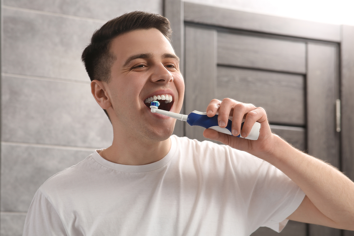 Man brushing his teeth with electric toothbrush in bathroom